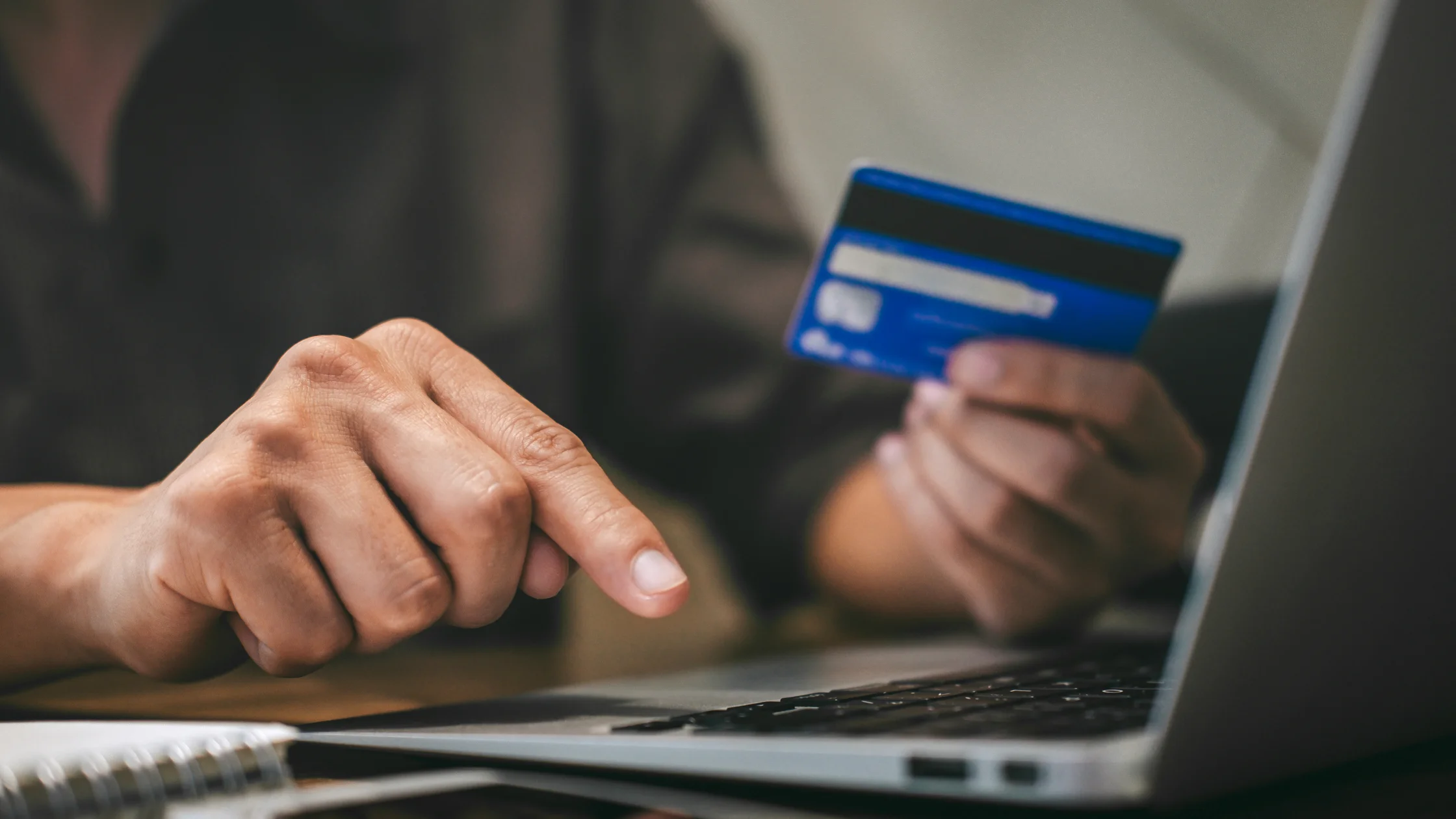 Close-up of hand holding card while using laptop for High-Risk Merchant Accounts.